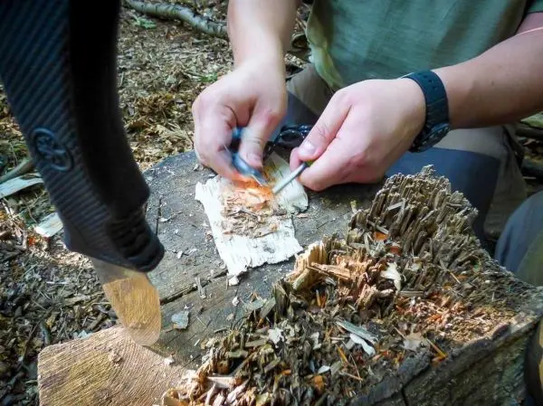 Feuerstahl erzeugt Funken auf Zunderstück auf Holzunterlage