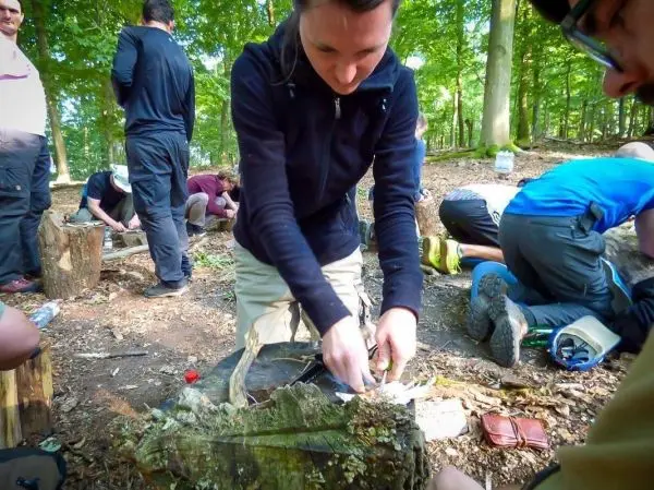 Frau bearbeitet Holzstück mit einem Messer in einem Waldgebiet