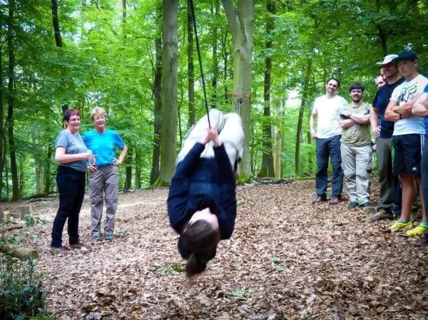 Frau überquert an einem Seil zwischen Bäumen, Zuschauer beobachten aufmerksam