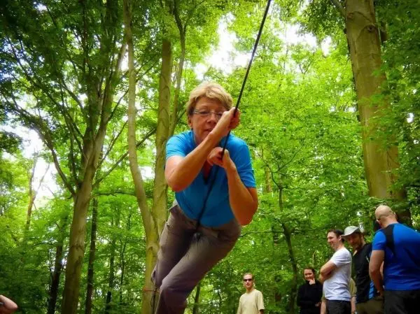 Frau überquert selbstgebaute Seilbrücke zwischen Bäumen im Wald
