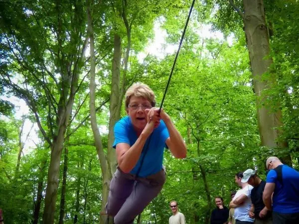 Frau überquert selbstgebaute Seilbrücke zwischen Bäumen im Wald