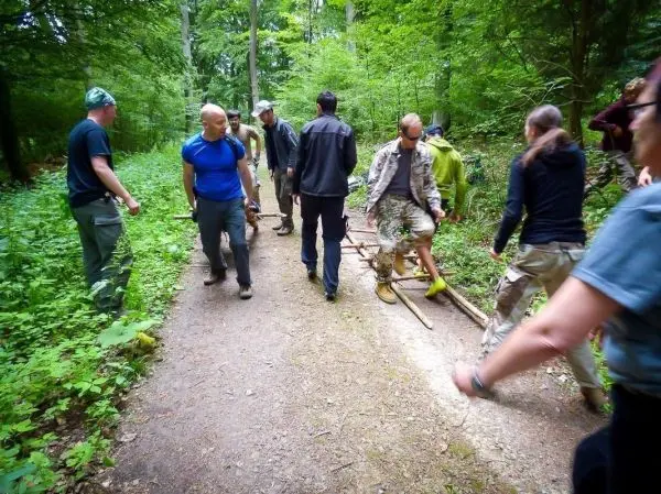 Gruppe transportiert improvisierte Trage aus Holzstücken auf einem Waldweg