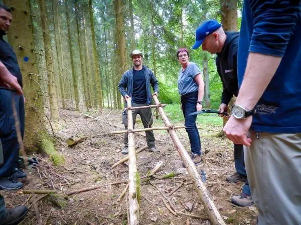 Gruppierung arbeitet an einer selbstgebauten Trage aus Holzstöcken im Wald
