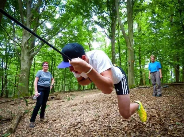 Junge überquert selbstgebaute Seilbrücke, während zwei Personen zuschauen