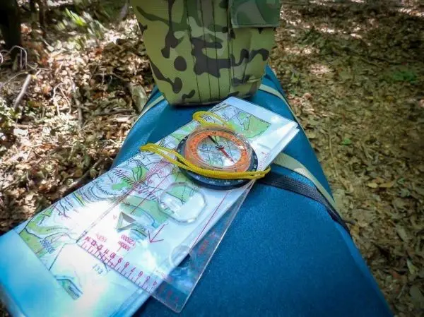 Karte und Kompass liegen auf einem Rucksack im Wald beim Überlebenstraining