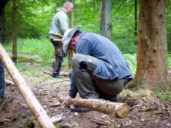 Mann bearbeitet Holzstück auf dem Boden im Wald