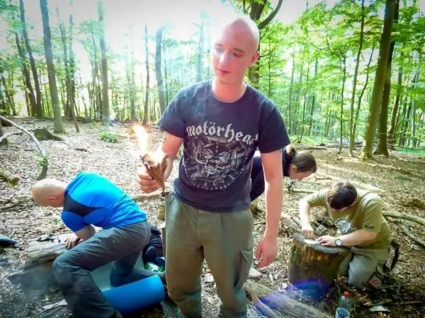 Mann hält brennendes Zundernest in der Hand, während andere am Boden arbeiten