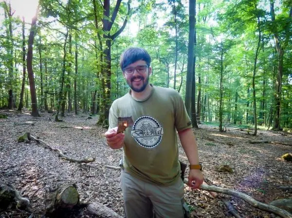 Mann hält ein Stück Holz in einem Wald mit vielen Bäumen