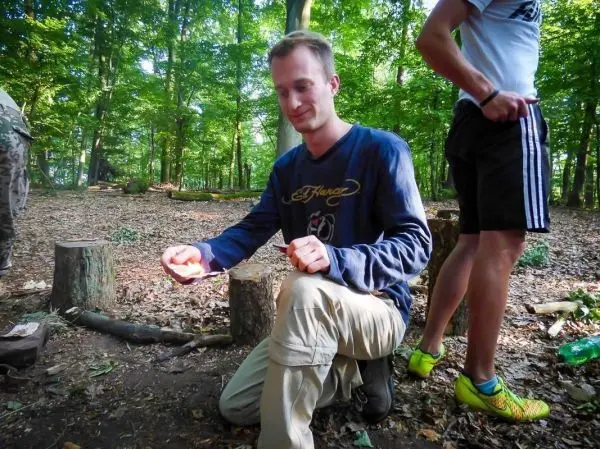 Mann kniet auf dem Boden und hält Zunder in der Hand