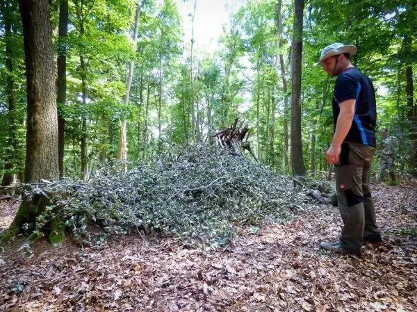 Mann steht neben einem Haufen aus Ästen und Laub im Wald