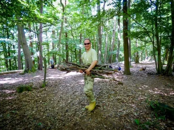 Mann trägt mehrere Äste durch den Wald, um Holz zu sammeln