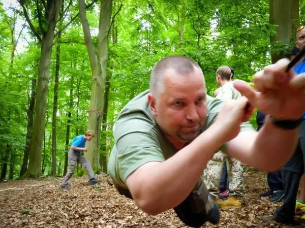 Mann überquert selbstgebaute Seilbrücke im Wald, während andere beobachten