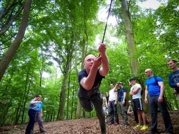 Mann überquert selbstgebaute Seilbrücke im Wald, Zuschauer beobachten
