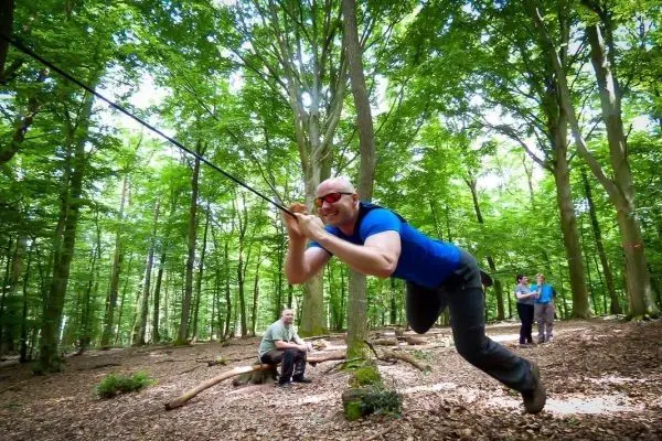 Mann überquert selbstgebaute Seilbrücke zwischen Bäumen im Wald
