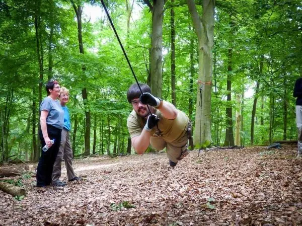 Mann überquert selbstgebaute Seilbrücke zwischen Bäumen im Wald