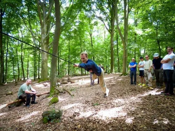 Mann überquert selbstgebaute Seilbrücke zwischen Bäumen, Zuschauer beobachten