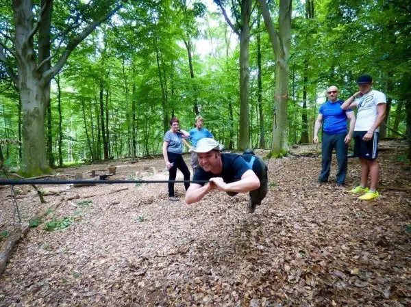 Mann überquert selbstgebaute Seilbrücke zwischen Bäumen, Zuschauer im Hintergrund