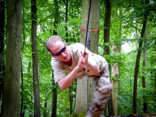 Mann überquert selbstgebaute Seilbrücke zwischen zwei Bäumen im Wald