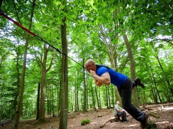 Mann überquert selbstgebaute Seilbrücke zwischen zwei Bäumen im Wald