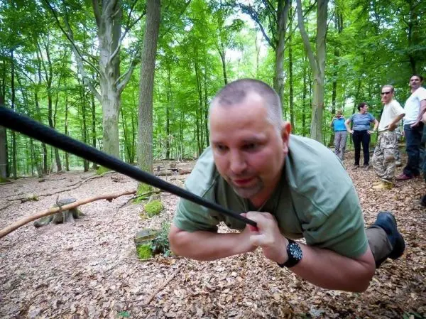 Mann zieht sich an einem Seil über den Waldboden, um eine Seilquerung zu üben