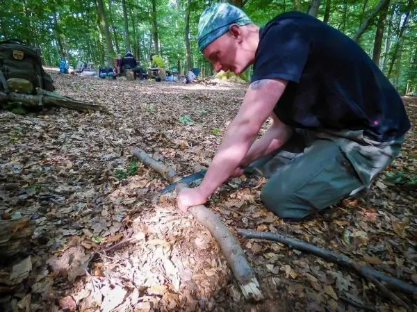Person bearbeitet einen Stock auf dem Boden im Wald beim Survival Training