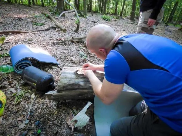 Person bearbeitet Holzstück auf einem Baumstamm beim Überlebenstraining