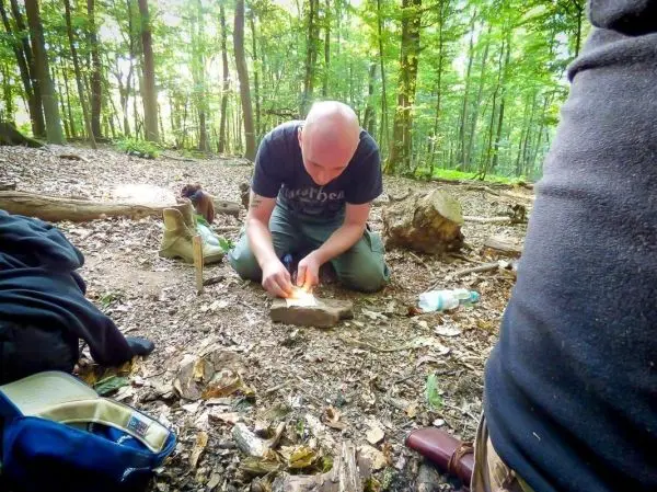 Person entzündet Feuer auf einem Holzstück im Wald beim Survival Training