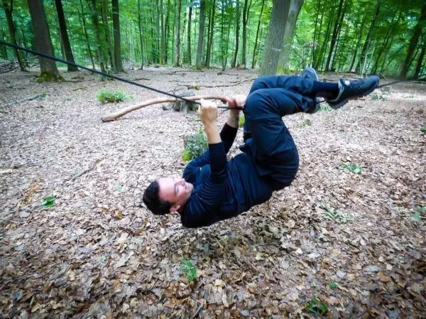 Person schwingt an einem Seil über den Boden im Wald