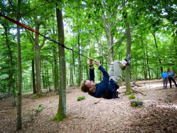 Person schwingt an Seil zwischen Bäumen im Wald beim Überlebenstraining