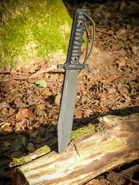 Schwarzes Messer steckt in einem Holzstück auf dem Waldboden