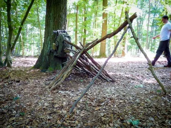 Selbstgebaute Tarp-Notunterkunft aus Ästen neben einem Baum