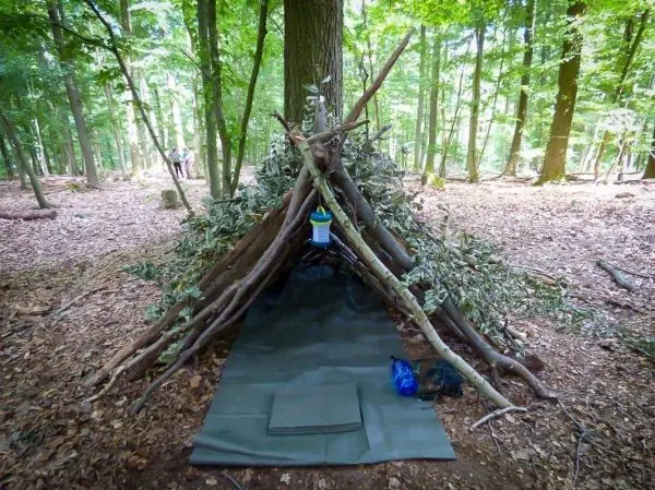 Selbstgebaute Tarp-Notunterkunft aus Ästen und Laub im Wald