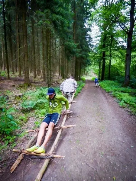 Selbstgebaute Trage mit zwei Personen im Wald auf einem Weg