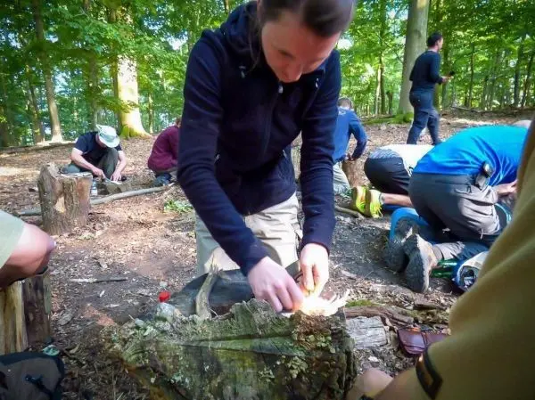 Zunder glimmt auf einem Holzstück während jemand mit einem Messer arbeitet