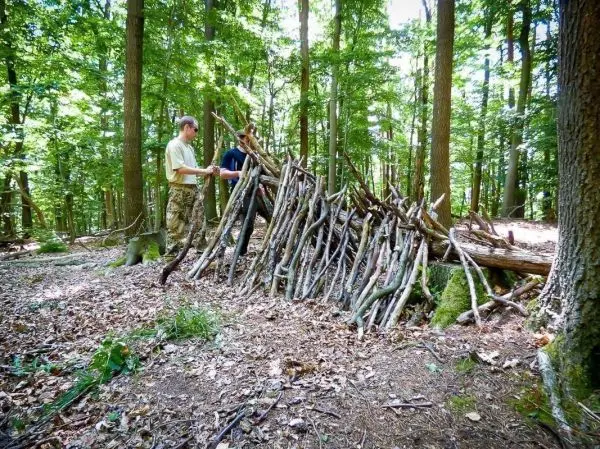 Zwei Personen bauen eine Holzunterkunft aus Ästen im Wald