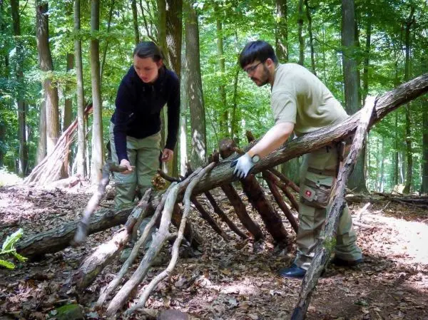 Zwei Personen bauen eine improvisierte Notunterkunft aus Ästen im Wald