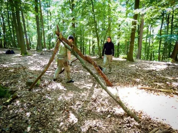 Zwei Personen bauen eine selbstgebaute Konstruktion aus Ästen im Wald