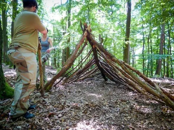 Zwei Personen bauen eine selbstgebaute Tarp-Notunterkunft aus Ästen im Wald