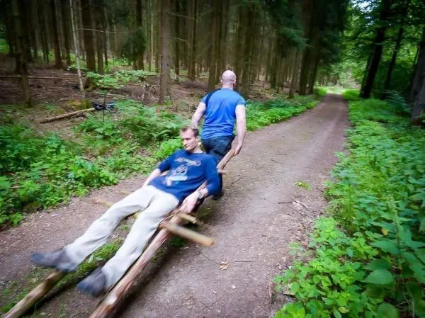 Zwei Personen nutzen eine selbstgebaute Holzschlittenkonstruktion auf einem Waldweg