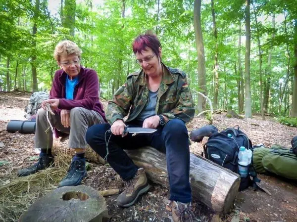 Zwei Personen sitzen auf einem Baumstamm und arbeiten mit Schnur
