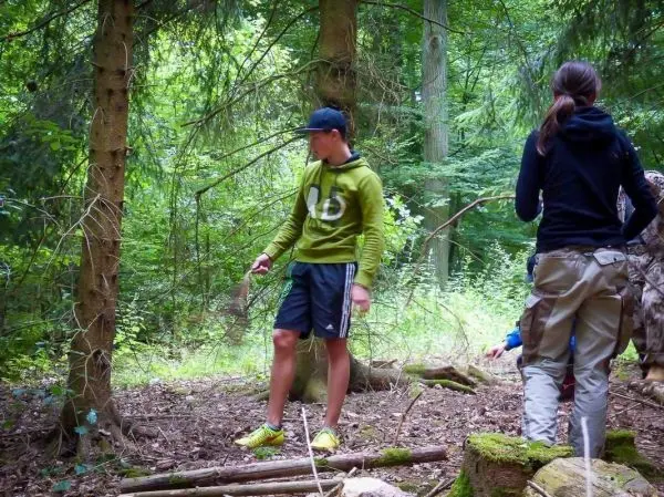 Zwei Personen stehen im Wald, einer hält einen Stock in der Hand