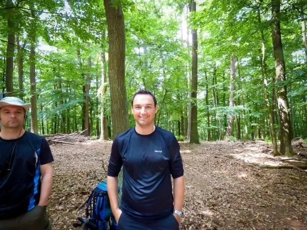 Zwei Personen stehen im Wald, umgeben von Bäumen und Laub
