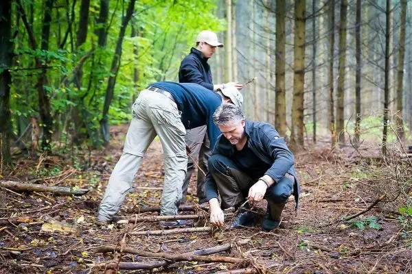 Drei Personen arbeiten im Wald an einer Holzstruktur aus Ästen