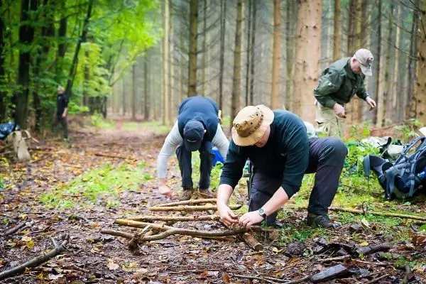 Drei Personen bauen eine selbstgebaute Konstruktion aus Ästen im Wald