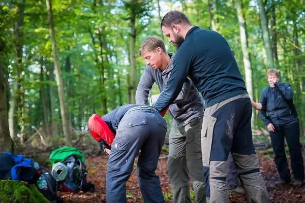 Drei Personen helfen einer Person beim Anlegen einer improvisierten Trage im Wald