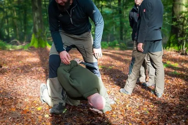 Eine Person wird im Wald am Boden gehalten, während andere Personen beobachten