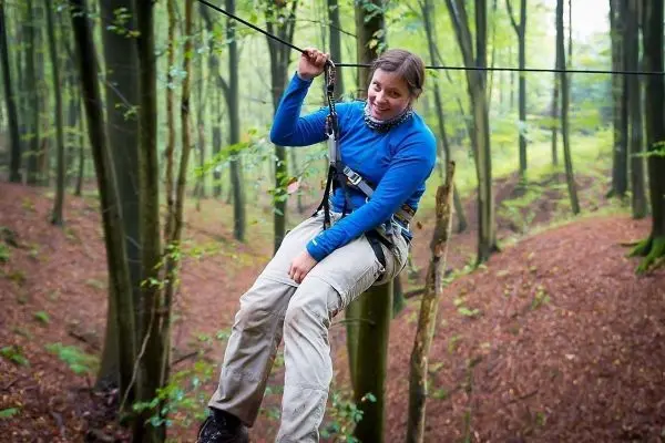 Frau hängt an einem Seil in einem Waldgebiet, gesichert mit einem Geschirr