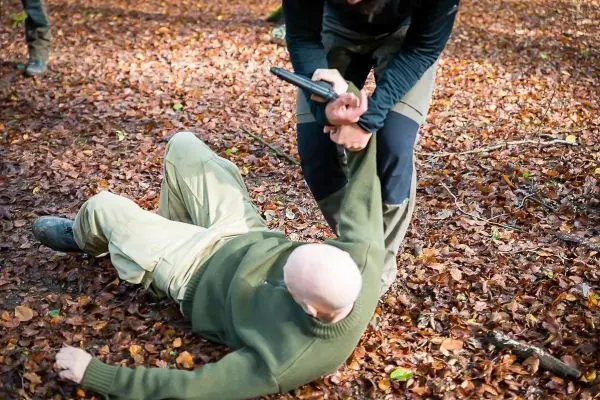 Kämpfer hält am Arm eines am Boden liegenden Mannes mit einer Waffe