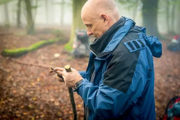 Mann bearbeitet einen Stock im Wald mit einem Messer