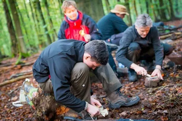 Mann bearbeitet Holzstück mit Messer auf dem Waldboden